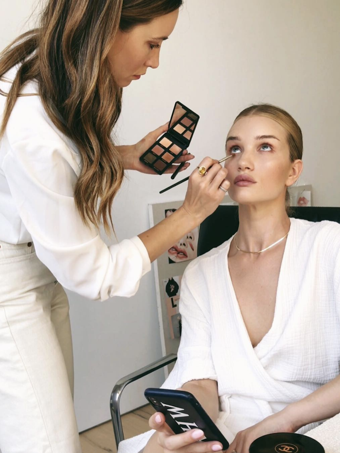 A professional makeup artist holding a eyeshadow pallete and doing a makeover of a model 